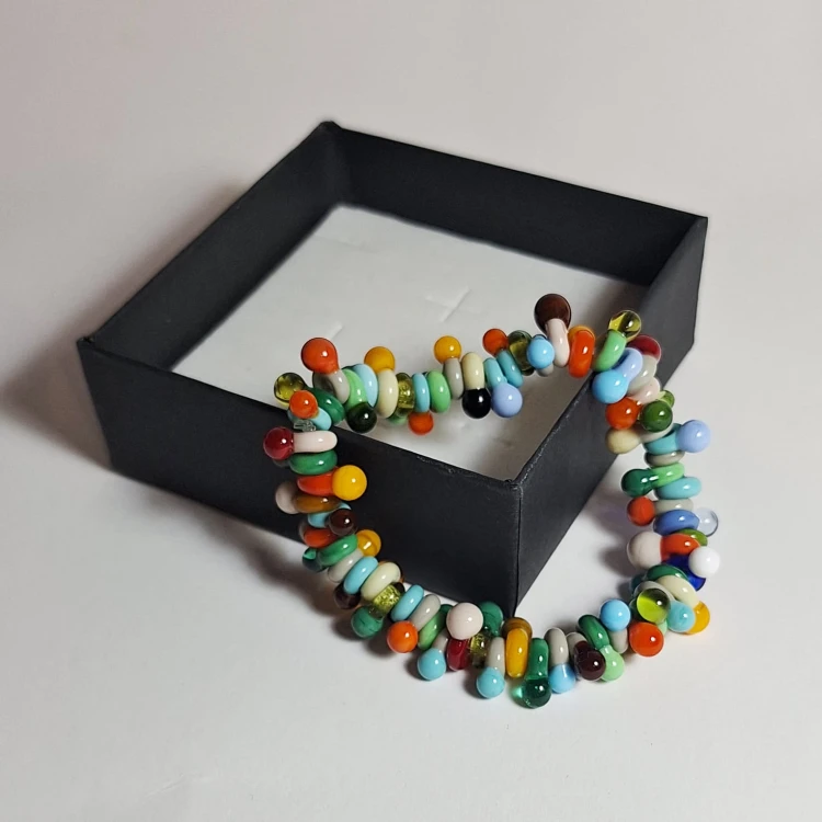 Ręcznie wykonana bransoletka ze szkła artystycznego lampwork. Tęczowe Marzenie oparta o róg pudełka