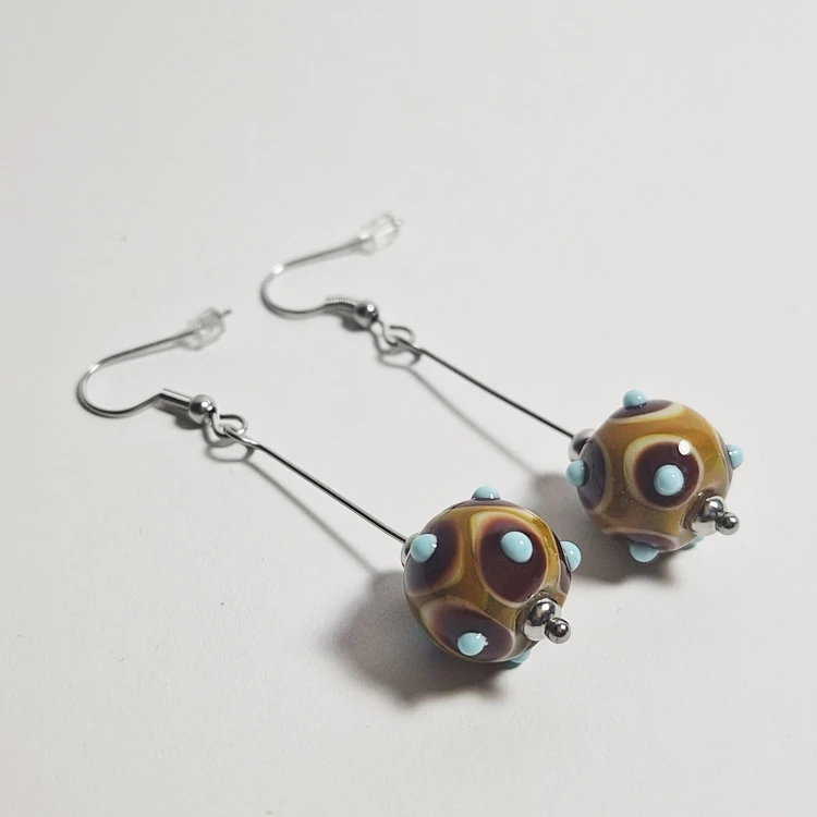 Karmelowe Krople ręcznie wykonane dwa kolczyki ze szkła artystycznego  lampwork  leżące obok siebie na stole