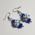 Błękitne Kwiaty ręcznie wykonane dwa kolczyki ze szkła artystycznego  lampwork  leżące obok siebie na stole