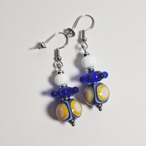 Słoneczne Fale ręcznie wykonane dwa kolczyki ze szkła artystycznego  lampwork  leżące obok siebie na stole