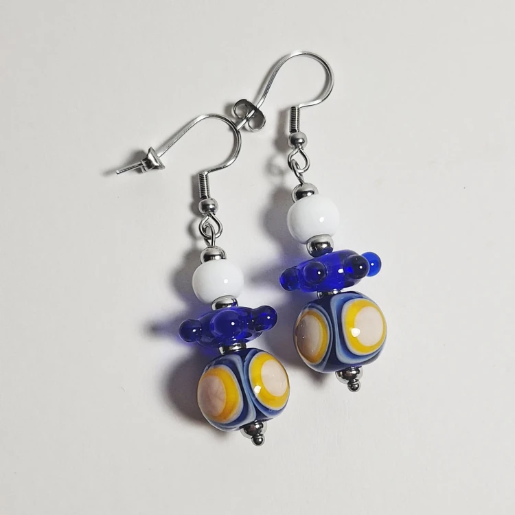 Słoneczne Fale ręcznie wykonane dwa kolczyki ze szkła artystycznego  lampwork  leżące obok siebie na stole